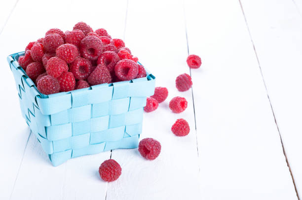 Fresh raspberries in a wicker basket on a white wooden background. Summer berries. Selective focus