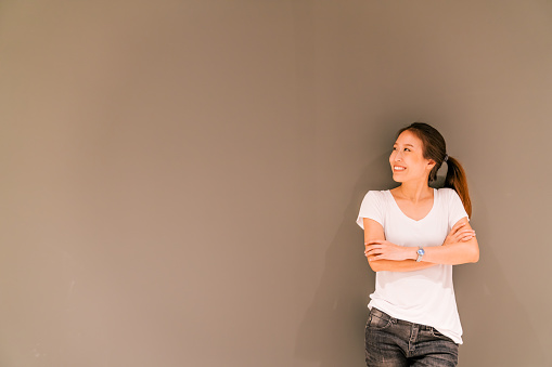 Beautiful Asian girl standing on grey wall background, looking at copy space