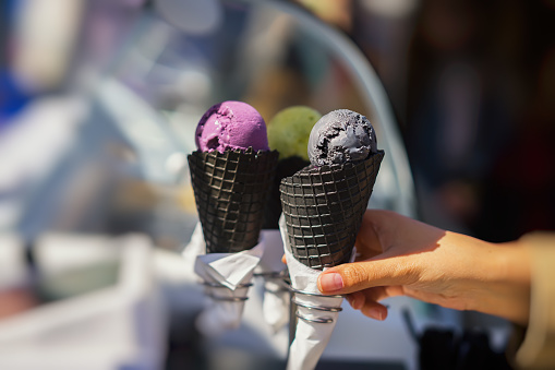 Close-up of three diverse Ice-cream in Black waffle cones. Close-up hand of the girl buyer. Real scene in the store. Selective focus. Copy space. For Background.