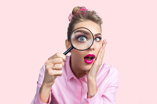 Funny image of young surprised female looking at the camera through a magnifying glass