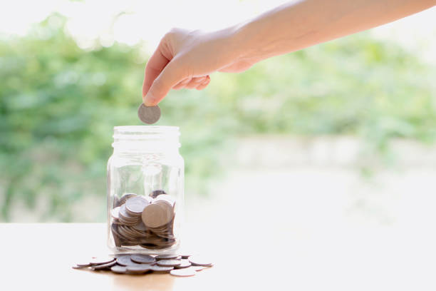 istock Woman Dropping Coins Into Glass Jar 692589954