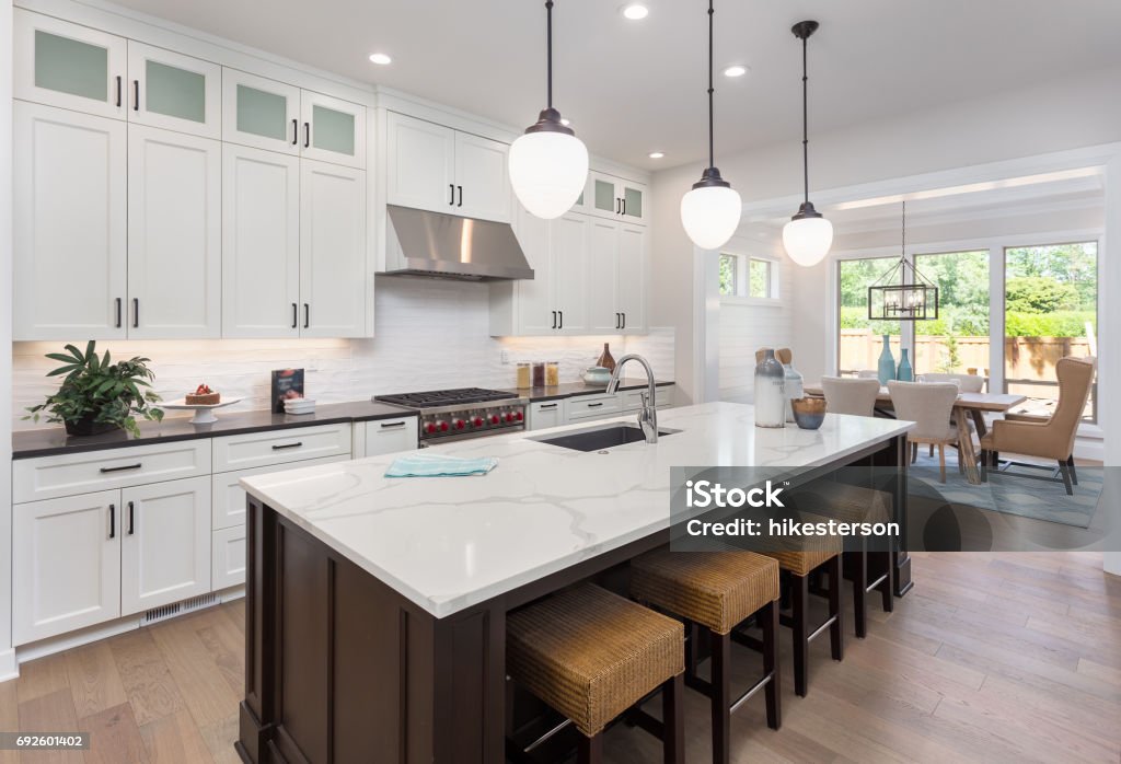 beautiful kitchen in new luxury home with island, pendant lights, and hardwood floors. Includes view of dining room. kitchen in newly constructed luxury home Kitchen Stock Photo