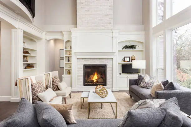 Photo of Beautiful living room interior with tall vaulted ceiling, loft area, hardwood floors and fireplace in new luxury home. Has large bank of windows
