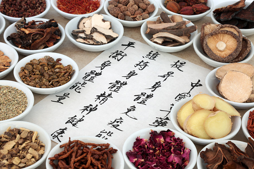 Traditional chinese medicinal herb selection in porcelain bowls with calligraphy script on rice paper. Translation describes chinese herbal medicine as increasing the bodys ability to maintain body and spirit health and balance energy.
