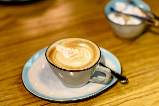istock Cup of cappuccino with a pattern and a sugar bowl with brown and white sugar are on the table 692638534