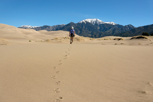 Leaving tracks in the dune, a woman hikes towards the snow covered Mount Herard in the Sangre de Cristo Mountains in the Great Sand Dunes National Park, Colorado.