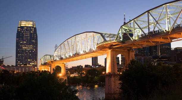 People Walk Across Cumberland River Pedestrian Bridge Nashville Tennessee Night falls as pedestrians walk across a bridge for an event footbridge stock pictures, royalty-free photos & images