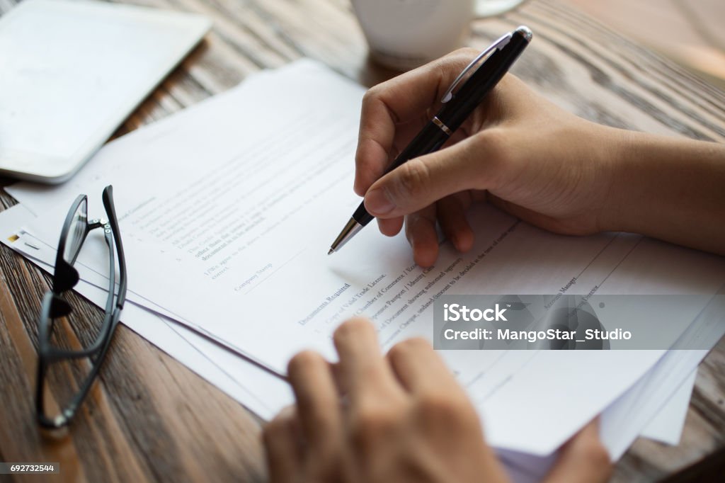 Businessman examining papers at table Unrecognizable businessman examining papers at table. Manager with ballpoint pen filling business papers. Close-up of male hands working at desk. Analyzing documents concept Application Form Stock Photo