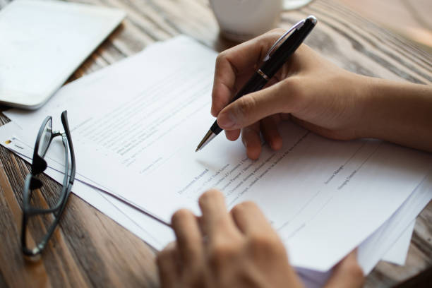 Businessman examining papers at table Unrecognizable businessman examining papers at table. Manager with ballpoint pen filling business papers. Close-up of male hands working at desk. Analyzing documents concept form submission stock pictures, royalty-free photos & images