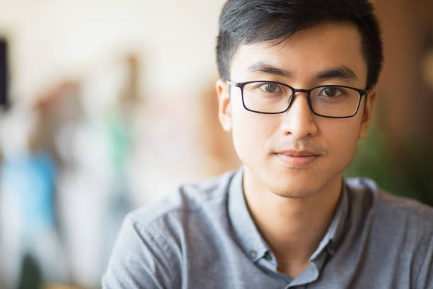 Portrait of confident Asian businessman in eyeglasses. Serious young manager looking at camera. Smart male student sitting alone. Young entrepreneur concept