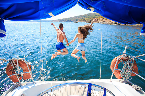 Rear view of couple holding hands and jumping into water from yacht.