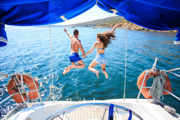 Rear view of couple jumping into ater Rear view of couple holding hands and jumping into water from yacht. sailing couple stock pictures, royalty-free photos & images