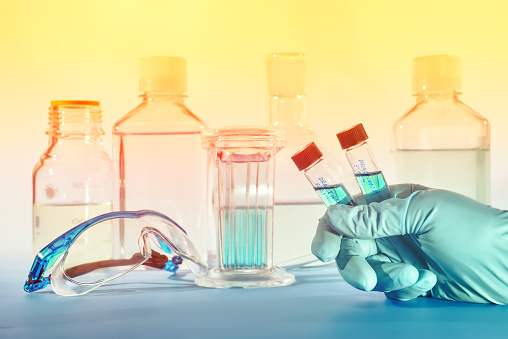Two liquid samples in plastic vials in the hand of female scientist, scientific background in blue and orange