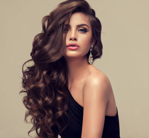 młoda atrakcyjna brunetka z obszerną, błyszczącą i kręconą fryzurą. - hairstyle long hair curly hair women zdjęcia i obrazy z banku zdjęć