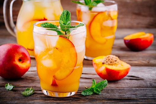 Summer cold drinks: homemade peach ice tea with ice cubes, and mint in glass on wooden background