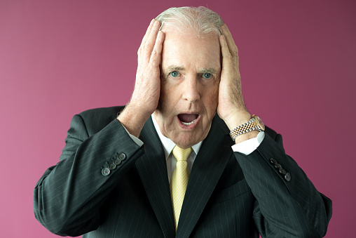 Closeup portrait of shocked senior business man clutching head with his mouth open. Isolated front view on purple background.