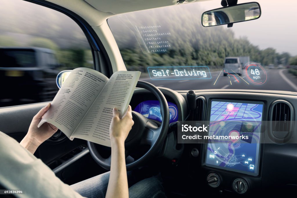 cabina di pilotaggio dell'auto a guida autonoma. un veicolo in modalità di guida autonoma e un libro di lettura del conducente donna. - Foto stock royalty-free di Auto senza conducente