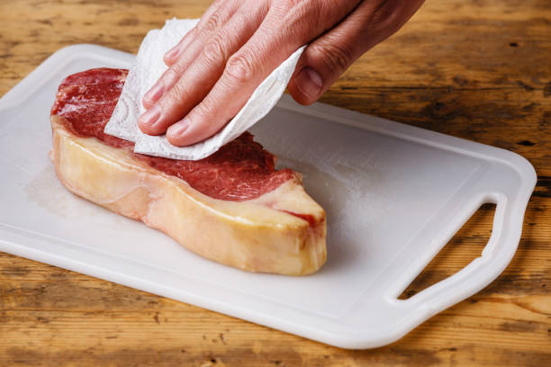 Raw meat Steak drying up excess moisture with paper towel Raw fresh meat Steak Striploin on cutting board drying up excess moisture by Male hand with paper towel paper towel photos stock pictures, royalty-free photos & images
