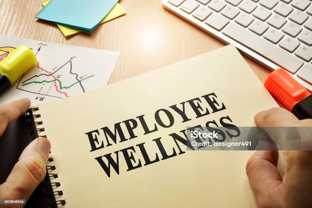 Hands holding documents with title Employee Wellness. Employee Stock Photo