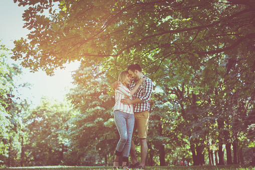 Young couple in hug walking on the meadow together.  Smiling couple looking each other.