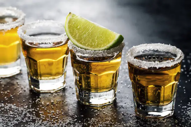 Tasty alcohol drink cocktail tequila with lime and salt on vibrant dark background. Closeup. Horizontal.