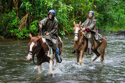 Man and woman galloping in River Arenal during Horseback riding on foot of  Volcano Arenal, Costa Rica.