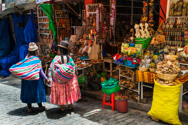 dos locales mujer vestida con ropa tradicional frente a una tienda en una calle de la ciudad de la paz, en bolivia - bolivian culture fotografías e imágenes de stock