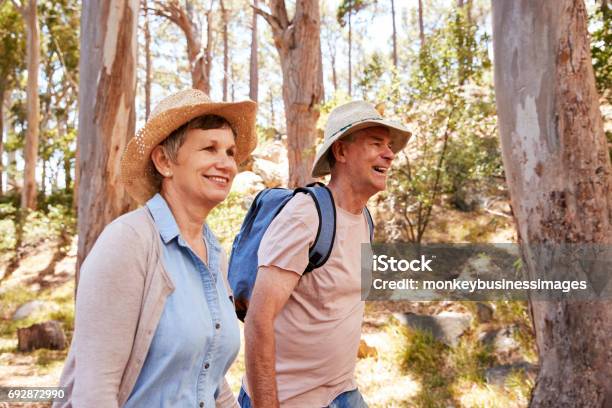 Mature Couple Hiking Along Forest Path Together Stock Photo - Download Image Now - Mature Couple, Hiking, Hat