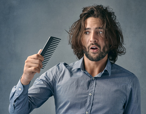 Shot of a handsome young man looking at the comb after combing his hair