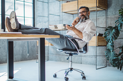 Businessman using phone with his feet up on the desk in an office