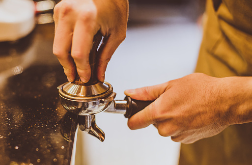 Close up shot of male waiters hand pressing tamper on ground coffee  in portafilter for making a coffee in cafe shop