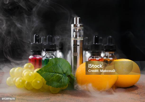 Electronic Cigarette Lemons And Bunch Of Grapes Within Vapor On Black Background Stock Photo - Download Image Now