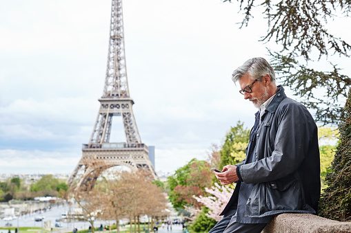 Shot of a handsome mature man using a cellphone in Paris with the Eiffel Tower in the background