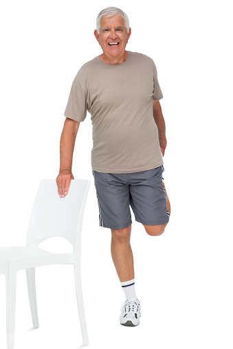 Full length portrait of a happy senior man stretching leg over white background