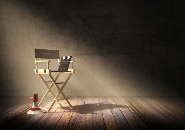 Photo of Director's chair with clapper board and megaphone in dark room