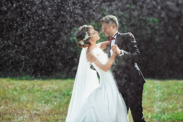 istock Bride and bridegroom embracing and smiling under rain 692915628