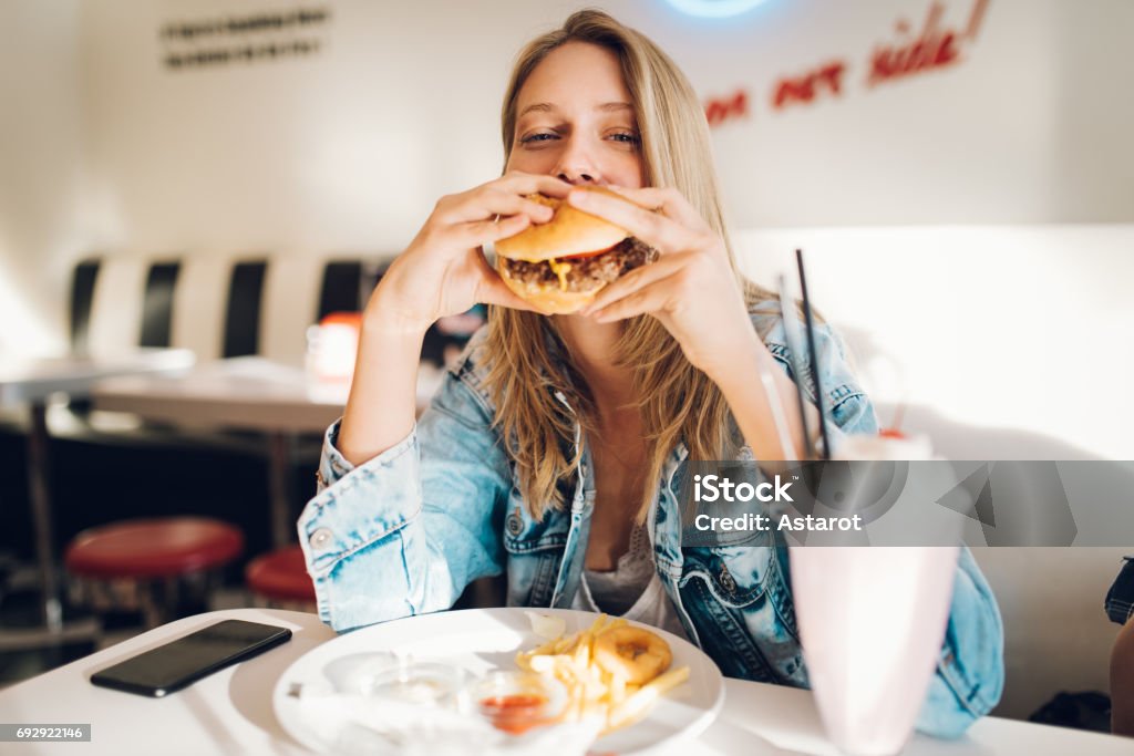 Food and drink Young woman eating burger in restaurant Eating Stock Photo