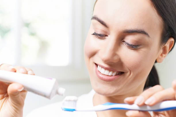 istock Woman Squeezing Toothpaste Onto Toothbrush In Bathroom 692923332