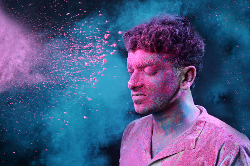 Young man smeared with colours plays Holi.Concept for Indian festival Holi.