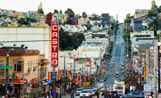 San Francisco Castro street Gay district city scene late Winter afternoon panoramic view with light traffic. The image features the Castro theater to the left, and many rainbow flags on each sides.