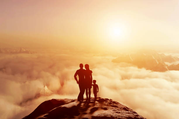 Family of three standing together on mountain and looking on cloudscape horizon at sunset. Parents and child, conceptual.