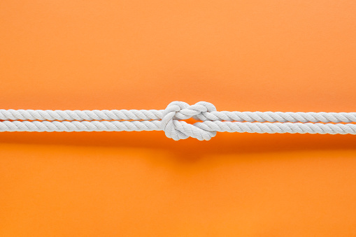 White ship ropes connected by reef knot. On orange background