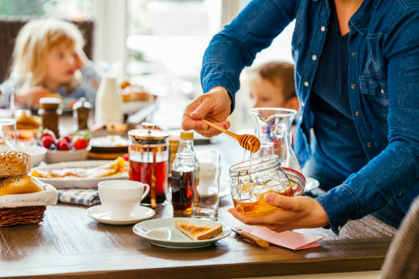 junge familie mit frühstück mit eiern, speck, joghurt mit frischen früchten - waffle syrup pouring breakfast stock-fotos und bilder