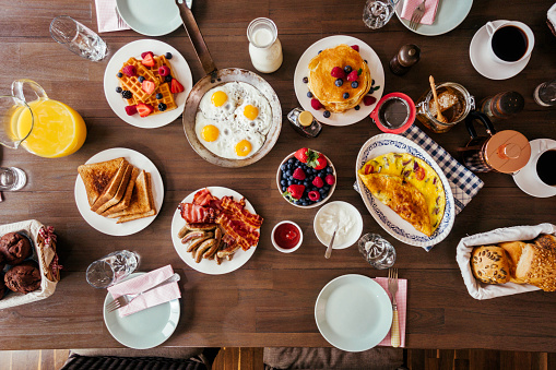 Having Breakfast with Eggs, Bacon, Yogurt with Fresh Fruits, Croissants, Toast with Honey and fresh Coffee