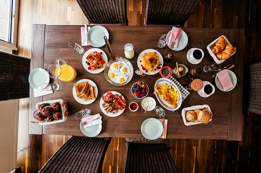 Having Breakfast with Eggs, Bacon, Yogurt with Fresh Fruits, Croissants, Toast with Honey and fresh Coffee