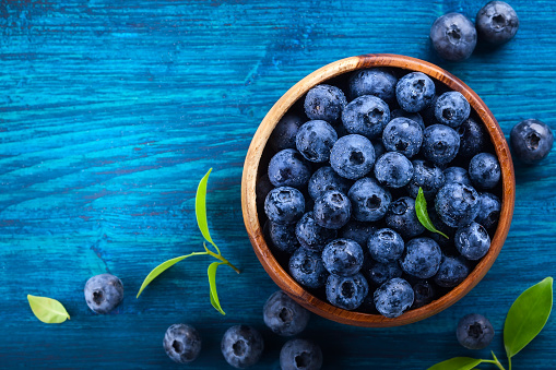 Fresh blueberry with drops of water in wooden bowl on blue  background. Top view. Concept of healthy and dieting eating