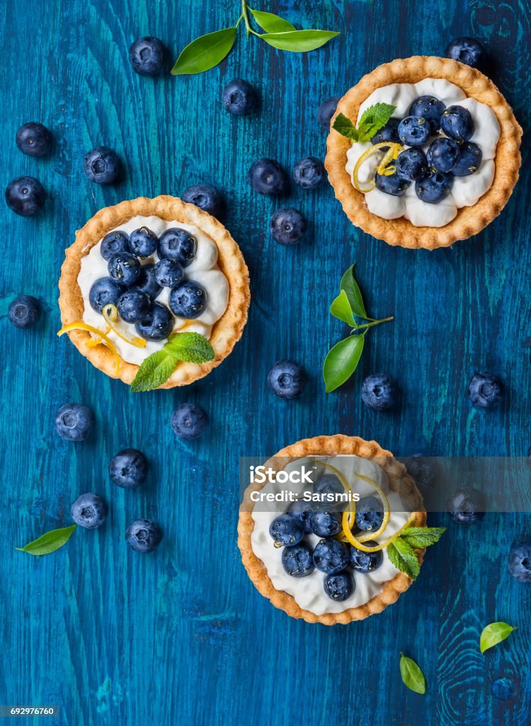 Blueberry tartlets Delicious Blueberry tartlets with vanilla cream on  blue wooden background. Top view. Blueberry Stock Photo