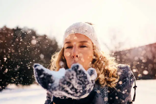Portrait of mid adult woman outdoor at winter time. Holding snow in arms and blowing snow
