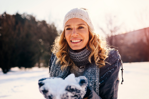 Portrait of mid adult woman outdoor at winter time. Holding snow in arms and smiling