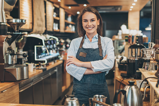 Smiling barista standing with arms crossed in a coffee shop